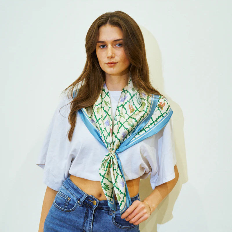 Woman wearing a floral scarf, white crop top, and blue jeans against a plain background