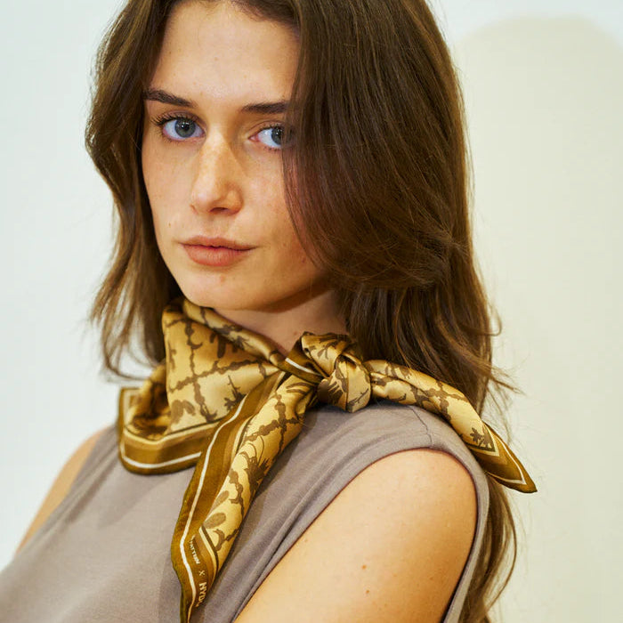Woman wearing a gold patterned scarf on a plain background