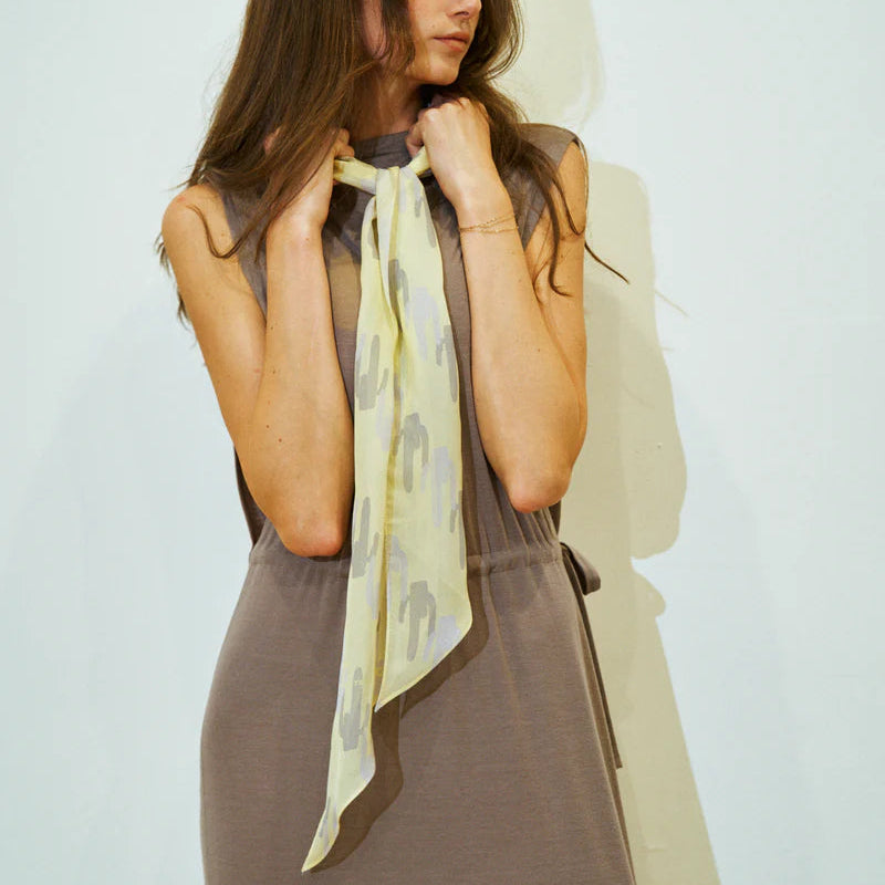 Woman wearing a light-colored scarf with a subtle pattern against a plain background