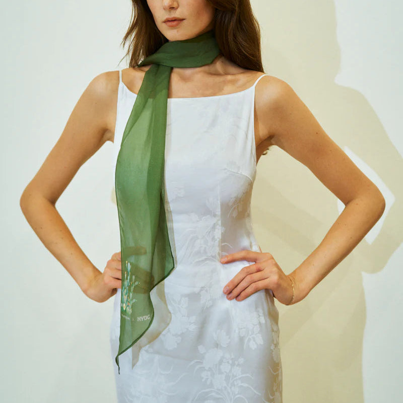 Woman wearing a green scarf over a white dress against a plain background