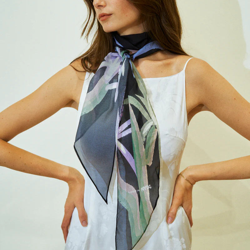 Woman wearing a white sleeveless top with a colorful scarf around her neck against a plain background