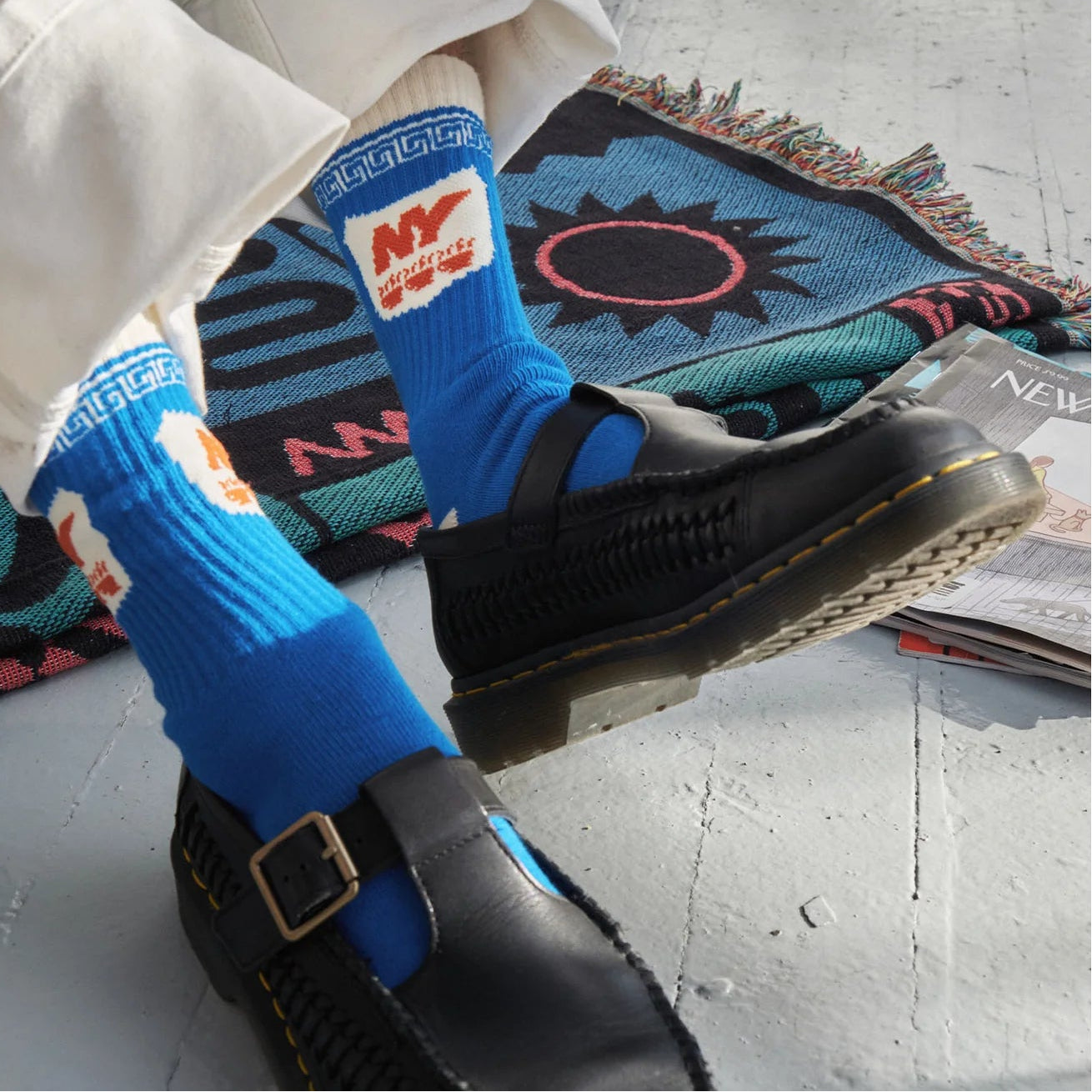 Person wearing blue socks with a logo and black shoes on a textured floor.